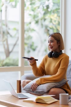 Young woman watching TV resting on sofa sitting in living room in house. Female watch film on television sitting on couch in apartment, leisure.