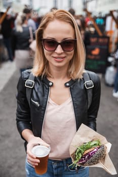 Beautiful young woman holding delicious organic salmon vegetarian burger and homebrewed IPA beer on open air beer an burger urban street food festival in Ljubljana, Slovenia