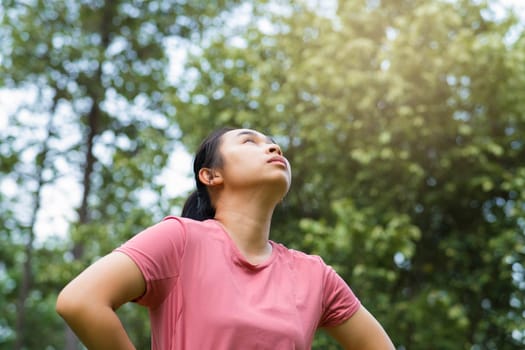 Portrait of young Asian woman in sportswear resting after jogging. Healthy young woman taking a break after jogging in the park. Healthy lifestyle concept.