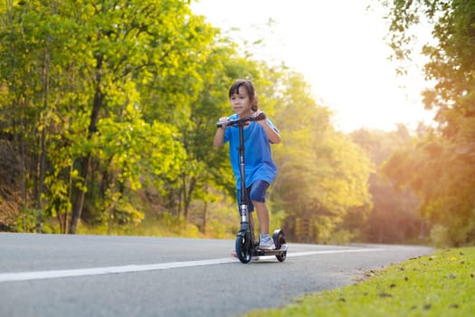 Active little girl riding a scooter on the road in the park on a summer day. Cute little girl wearing helmet enjoys riding kick scooter in outdoor park. Leisure activities and outdoor sports for children.