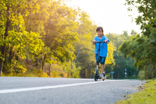 Active little girl riding a scooter on the road in the park on a summer day. Cute little girl wearing helmet enjoys riding kick scooter in outdoor park. Leisure activities and outdoor sports for children.