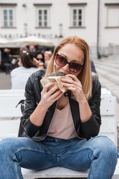 Pretty young blonde funny woman eating hamburger outdoor on the street