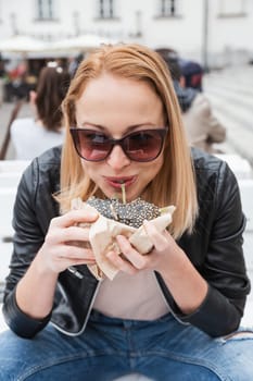 Pretty young blonde funny woman eating hamburger outdoor on the street