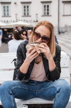 Pretty young blonde funny woman eating hamburger outdoor on the street