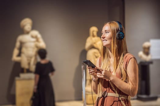 Portrait of contemporary young woman looking at sculptures and listening to audio guide at museum exhibition.
