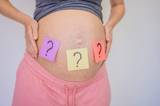 Choosing baby name. Confused pregnant woman with question marks on paper stickers on tummy.