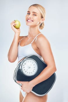 Health, diet and woman with scale and apple to lose weight for health, wellness and healthy lifestyle as fitness mockup studio background. Portrait, smile and body of model eating fruit for nutrition.