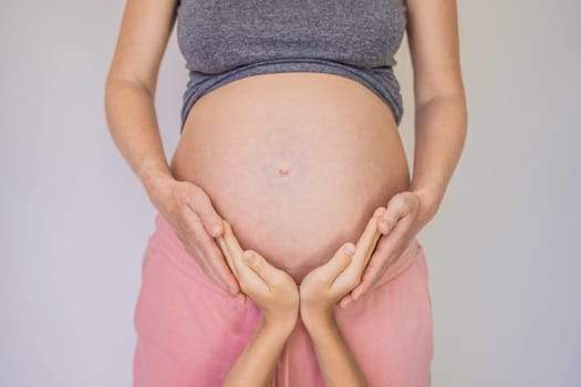 Young beautiful pregnant woman and eldest son. The cute boy put his hands on his mother's belly. Expecting a baby in the family concept. Preparing an older child for a younger one.