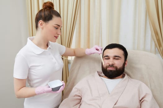 Bearded man getting laser facial treatment by professional cosmetologist in a beauty clinic. Healthy man lifestyle concept