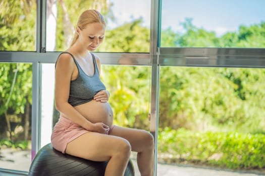 Pregnant woman exercising on fitball at home. Pregnant woman doing relax exercises with a fitness pilates ball. Against the background of the window.