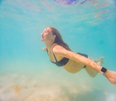 Pregnant woman underwater swimming in tropical sea. Healthy and active pregnancy. Young expecting mom on summer beach vacation before baby birth. Swim holiday and water fun. Travel during pregnancy. Underwater photography.