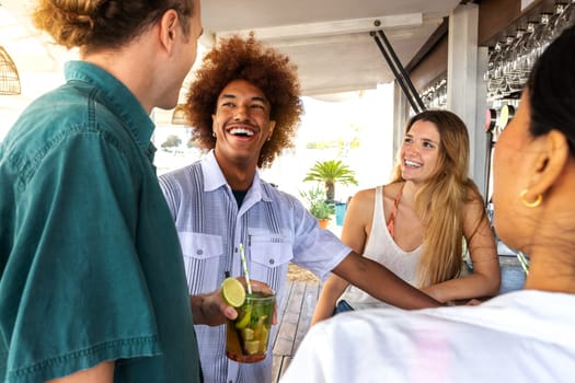 Happy diverse friends drinking mojito cocktails at a beach bar. Friends talking, laughing and having fun. Summertime lifestyle concept.