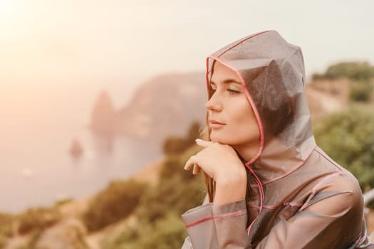 Woman rain park. Happy woman portrait wearing a raincoat with transparent umbrella outdoors on rainy day in park near sea. Girl on the nature on rainy overcast day