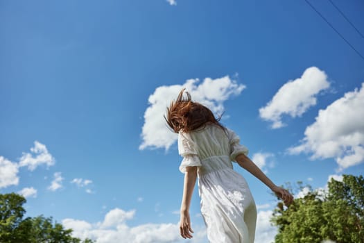 a woman in a light dress against a blue sky stands with her back to the camera. Photo from below. High quality photo