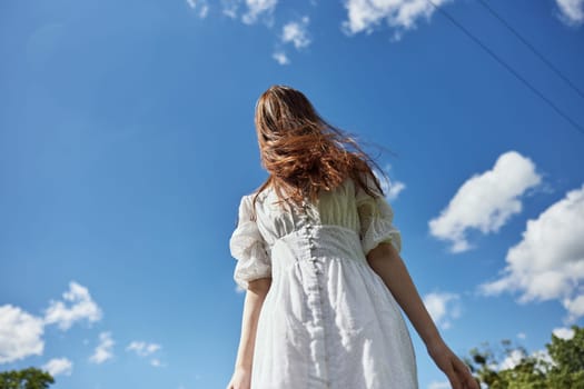 a woman in a light dress against a blue sky with hair covering her face. Photo from below. High quality photo