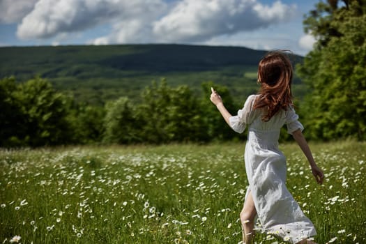 a free woman in a light dress runs through a field of daisies with her back to the camera. High quality photo