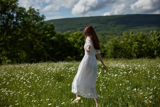 a free woman in a light dress runs through a field of daisies with her back to the camera. High quality photo