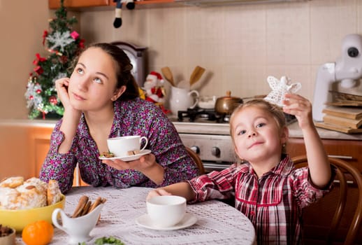 Two cute happy girls play at home. Funny lovely sisters are having fun in kitchen. Girls play tea-party. Two happy children, cute sisters, enjoying a tea party playing with dishes, cup cakes and muffins