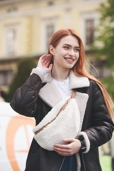 a red-haired girl in a leather jacket. cheerful woman with long red hair poses for a photographer.