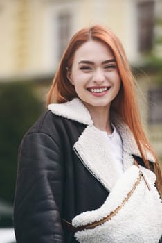 a red-haired girl in a leather jacket. cheerful woman with long red hair poses for a photographer.