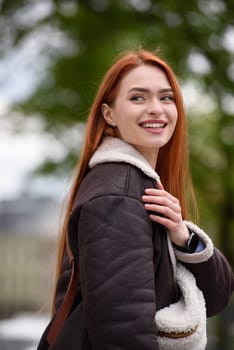 a red-haired girl in a leather jacket. cheerful woman with long red hair poses for a photographer.