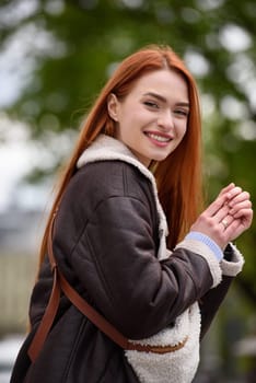 a red-haired girl in a leather jacket. cheerful woman with long red hair poses for a photographer.