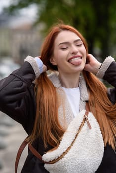 a red-haired girl in a leather jacket. cheerful woman with long red hair poses for a photographer.