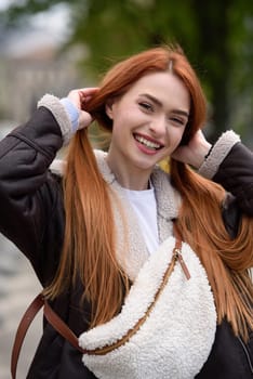 a red-haired girl in a leather jacket. cheerful woman with long red hair poses for a photographer.