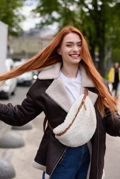 a red-haired girl in a leather jacket. cheerful woman with long red hair poses for a photographer.