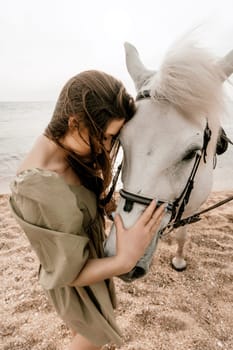 A woman in a dress stands next to a white horse on a beach, with the blue sky and sea in the background