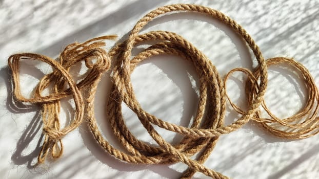 Jute twisted rope lying on a white surface with shadows from the sun. Abstract background, texture, pattern, frame