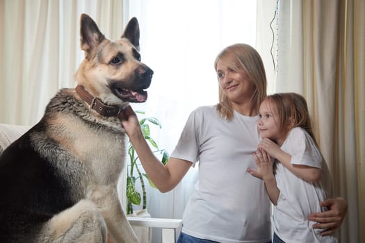 Happy loving family with mother, daughter and big dog in living room. Pet chephers, woman mom and small child girl who is afraid of a dog taken from a shelter