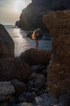 Woman tourist enjoying the sunset over the sea mountain landscape. Sits outdoors on a rock above the sea. She is wearing jeans and a blue hoodie. Healthy lifestyle, harmony and meditation.