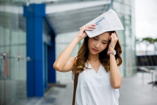 An Asian woman uses a newspaper to cover her face, feeling the damaging effects of city pollution and sun exposure on her skin and health.