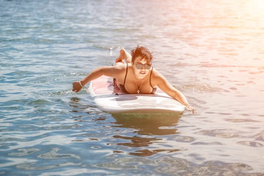 Woman sup sea travel. Sports girl on a surfboard in the sea on a sunny summer day. In a black bathing suit, he sits on a sapa in the sea. Rest on the sea