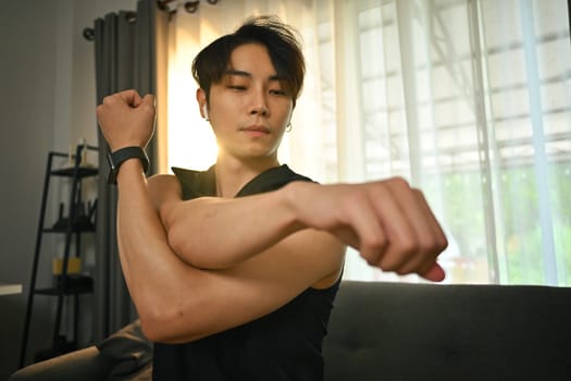 Handsome muscular man in sportswear stretching his arms, warming up exercises before working out at home.