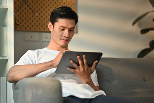 Handsome millennial man using digital tablet, checking email in morning, remote working from home.