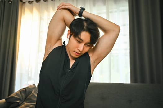 Young fitness man stretching arms during morning workout at home. Healthy lifestyle and sport concept.
