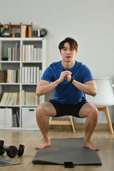 Full length of sporty male working out in the morning at home, doing squats exercise. Healthy lifestyle concept.