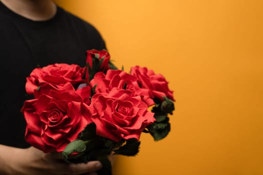 Man hands holding bouquet of red roses over yellow background with space for text.