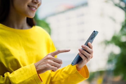 Pleasant young woman texting messages, chatting in social on smartphone while standing outdoor.