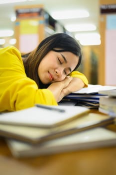 Tired exhausted young student sleeping on the table in library with pile of books. Education, prepare to exam, lesson.