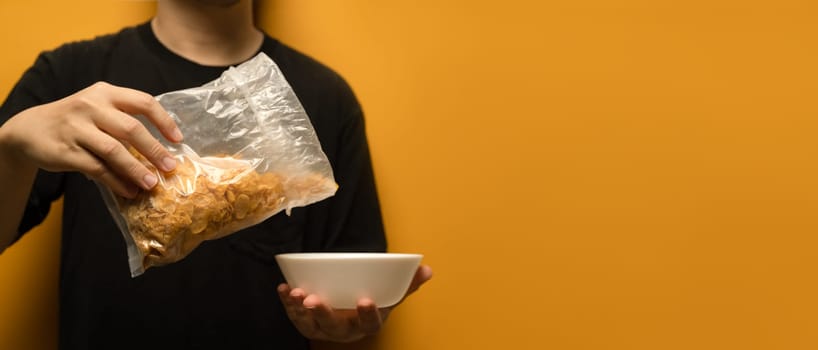 Man pouring cereals into a white bowl isolated on yellow background with space for advertising text message.