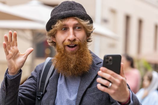 Oh my God Wow. Excited happy joyful winner young adult man use smartphone typing browsing celebrating win good message news. Redhead bearded guy with mobile phone walking in urban city street outdoors