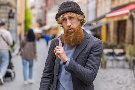 Displeased upset young bearded man reacting to unpleasant awful idea, dissatisfied with bad quality, wave hand, shake head No, dismiss idea, dont like proposal outdoors. Guy walking in city street