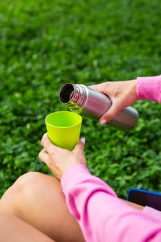 Girl traveler pours tea from a thermos, on the street. A woman pours a hot drink into a mug from a thermos