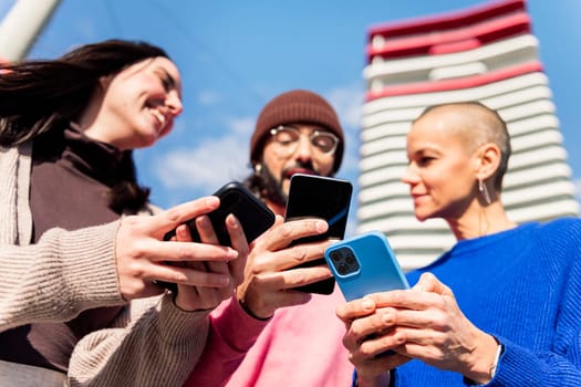 three young friends having fun using mobile phones at city, focus on the hands, concept of modern urban lifestyle and technology of communication, copy space for text