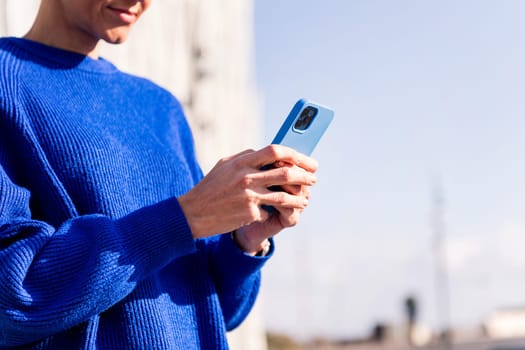 close-up of the hands of an unrecognizable woman with blue jersey using phone, concept or modern lifestyle and technology of communication, copy space for text