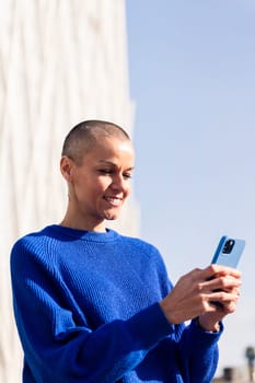 confident woman in blue sweater using mobile phone at city, concept or modern lifestyle and technology of communication, copy space for text
