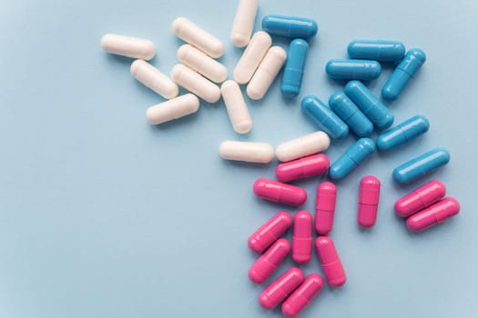 Various colored pills - blue, pink, white, falling out of a plastic bottle, isolated on a blue background